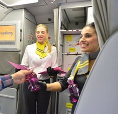 two women shaking hands on an airplane with another woman standing next to them and the man in the background