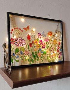 an art piece is displayed on top of a shelf with string lights and flowers painted on it