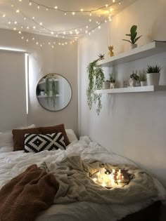 an unmade bed with some plants on the headboard and lights hanging above it