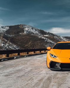 an orange sports car parked on the side of a road in front of snow covered mountains