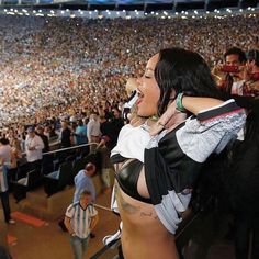 a woman is standing in front of an audience at a sporting event and singing into a microphone