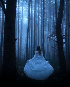 a woman in a white dress is walking through the woods with her back to the camera