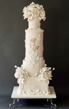 a three tiered wedding cake with white flowers on the top and bottom, sitting on a stand