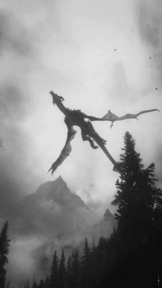 a black and white photo of a dragon flying in the air over trees with mountains in the background