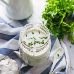 a glass jar filled with white sauce next to some parsley on a blue and white towel