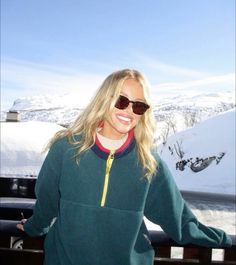 a woman wearing sunglasses standing in front of snow covered mountains