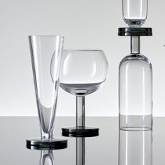 three glass vases and one empty wine glass on a table top with white walls in the background