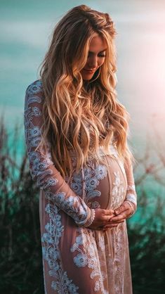 a pregnant woman standing in front of the ocean with her hands on her stomach and looking down