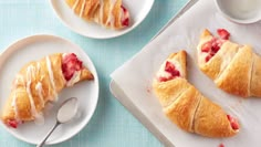 two white plates with pastries on them next to a cup of milk and spoon