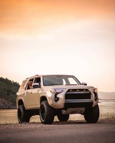 the toyota truck is parked on the side of the road by the water at sunset