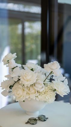 a white vase filled with lots of flowers on top of a table next to sunglasses