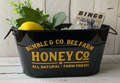 a bucket filled with fruit and vegetables sitting on top of a wooden table next to a sign