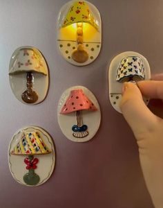 a person is pointing at some miniature hats on magnets that are attached to a wall