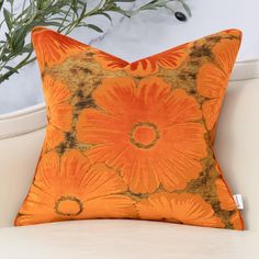 an orange floral pillow sitting on top of a white couch next to a potted plant