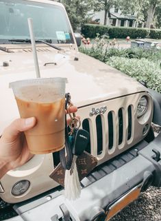 a hand holding a drink in front of a jeep with a key chain attached to it