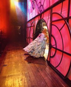 a woman in a long dress walking down a wooden floor next to a red wall