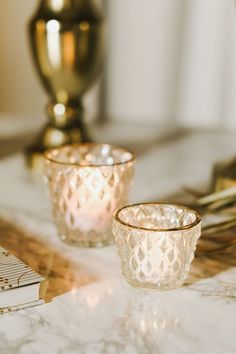 two clear glass cups sitting on top of a table next to a gold candle holder