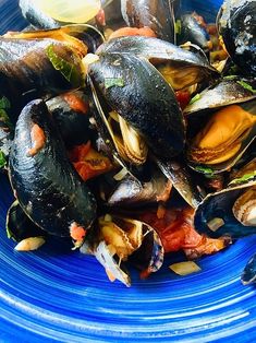 a blue plate filled with mussels and other food on top of a table