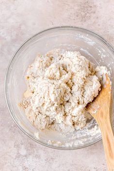 a wooden spoon in a glass bowl filled with flour and other ingredients for making bread