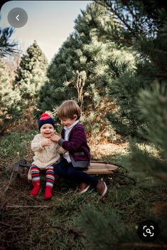 two young boys sitting on top of a skateboard in the grass next to trees