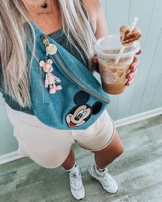 a woman is holding a drink in her hand and wearing mickey mouse shirt with white shorts