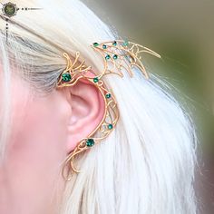 a woman with white hair wearing a gold and green dragon ear cuff on top of her head