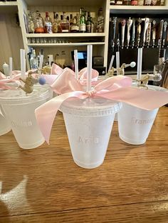 three plastic cups with pink bows on them sitting on a table in front of bottles