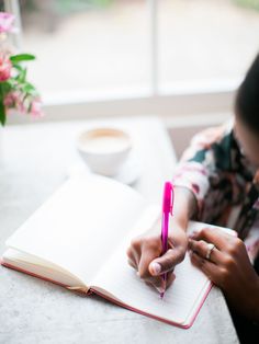 a person sitting at a table with a book and pen in their hand while writing