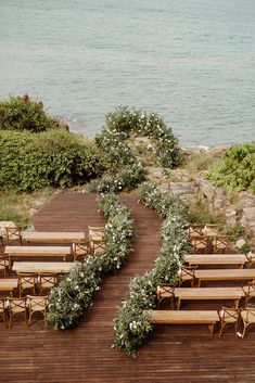 rows of wooden benches sitting on top of a wooden deck next to the ocean with greenery