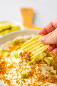 a hand holding a cracker over a bowl of dip with celery and cheese