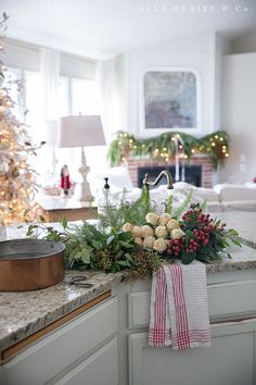 a kitchen counter with flowers and greenery on it in front of a christmas tree