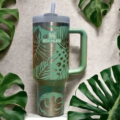 a green travel mug sitting on top of a counter next to some plants and leaves