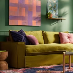 a living room with green walls and colorful art hanging on the wall above the couch