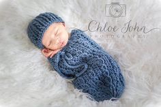 a newborn baby wearing a blue knitted outfit and sleeping on a fluffy white blanket