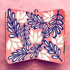 an orange and blue box with white leaves on it sitting against a pink wall next to a plant