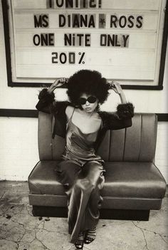 a black and white photo of a woman sitting on a couch in front of a sign