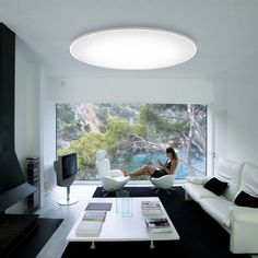 a woman sitting on a white couch in a living room with a large window looking out onto the outdoors