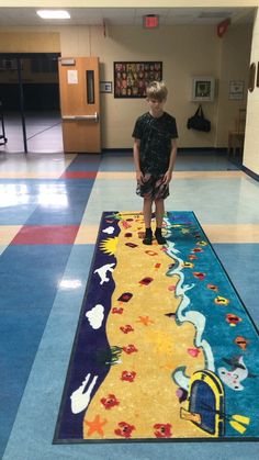 a young boy standing on top of a colorful rug in a school hallway next to a blue floor