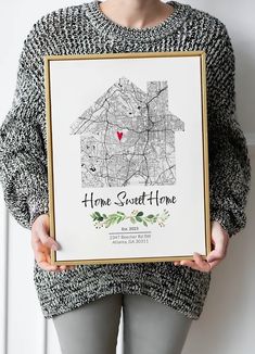 a woman holding up a framed home sweet home map