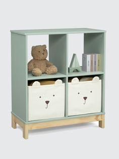 a teddy bear sitting on top of a book shelf next to two storage bins