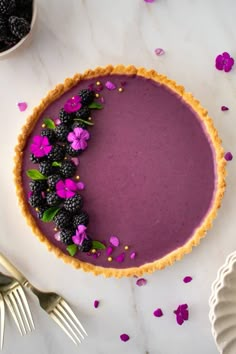 a purple dessert with blackberries and flowers on the top is ready to be eaten