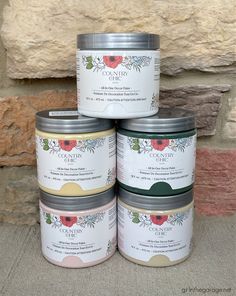 four tins of paint sitting next to each other in front of a stone wall