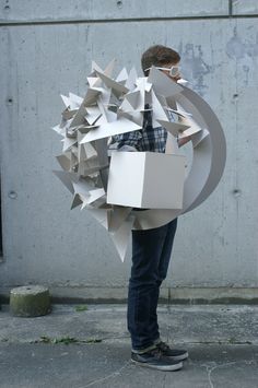 a man is standing on the sidewalk holding an object made out of boxes and paper