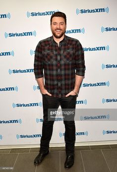 a man in plaid shirt and black pants standing on a blue carpet with his hands in his pockets