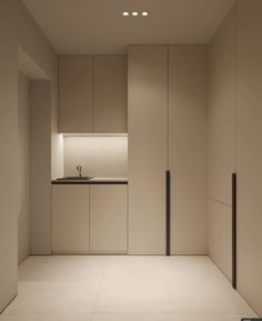 an empty room with white walls and cabinets in the corner, lights on above the sink