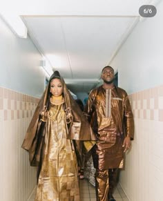 two people dressed in gold and black walking down a hallway