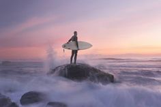 a person standing on top of a rock with a surfboard