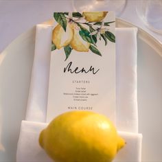 a lemon sitting on top of a white plate next to a place card and napkin