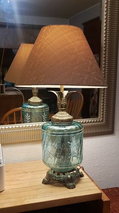 a lamp sitting on top of a wooden table next to a mirror with a reflection in it