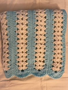 a blue and white crocheted blanket laying on top of a bed next to a pillow